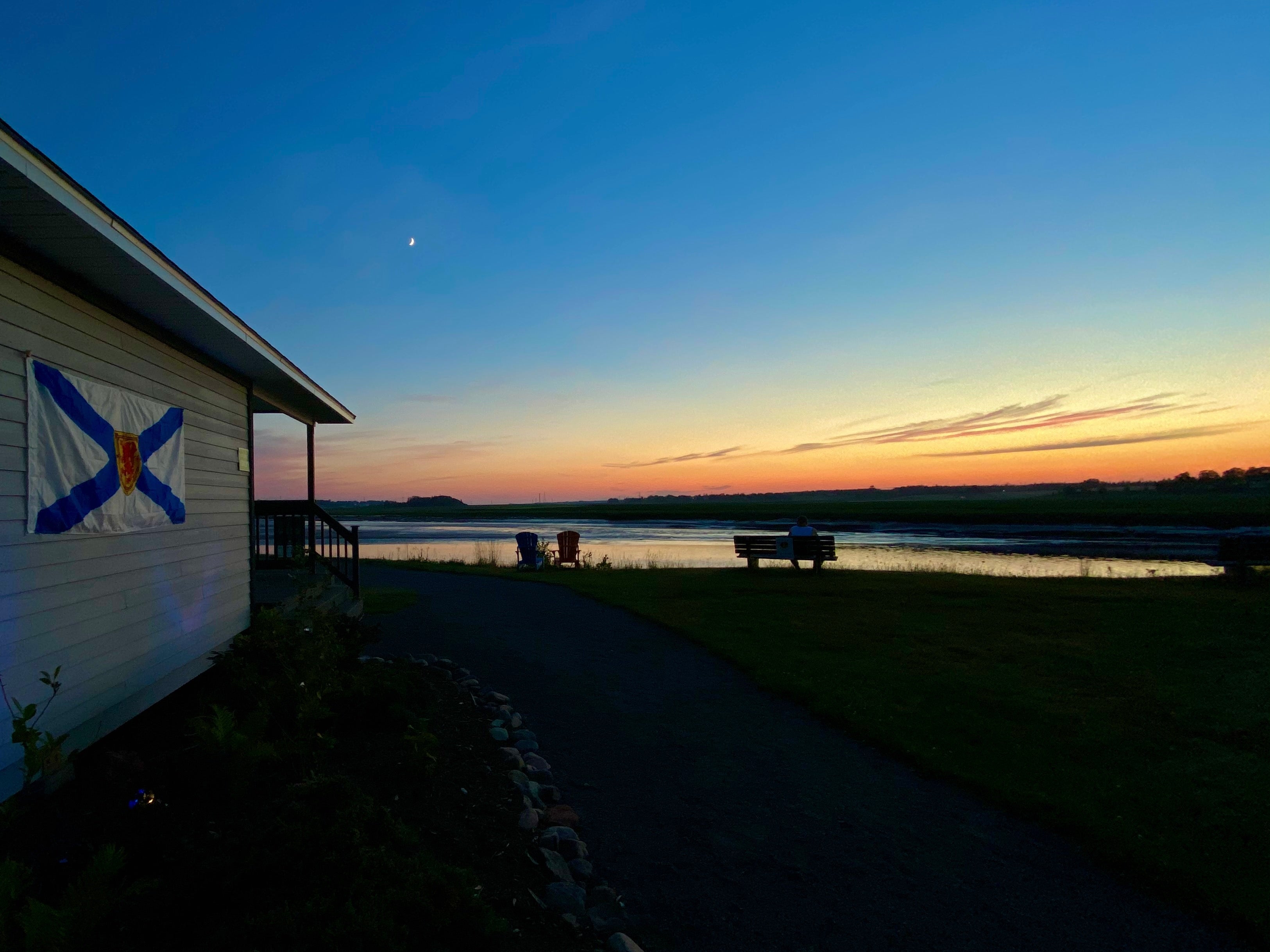 Sunset over the bay of fundy with a cresent moon and the side of a building with a Nova Scotia flag attached to it.